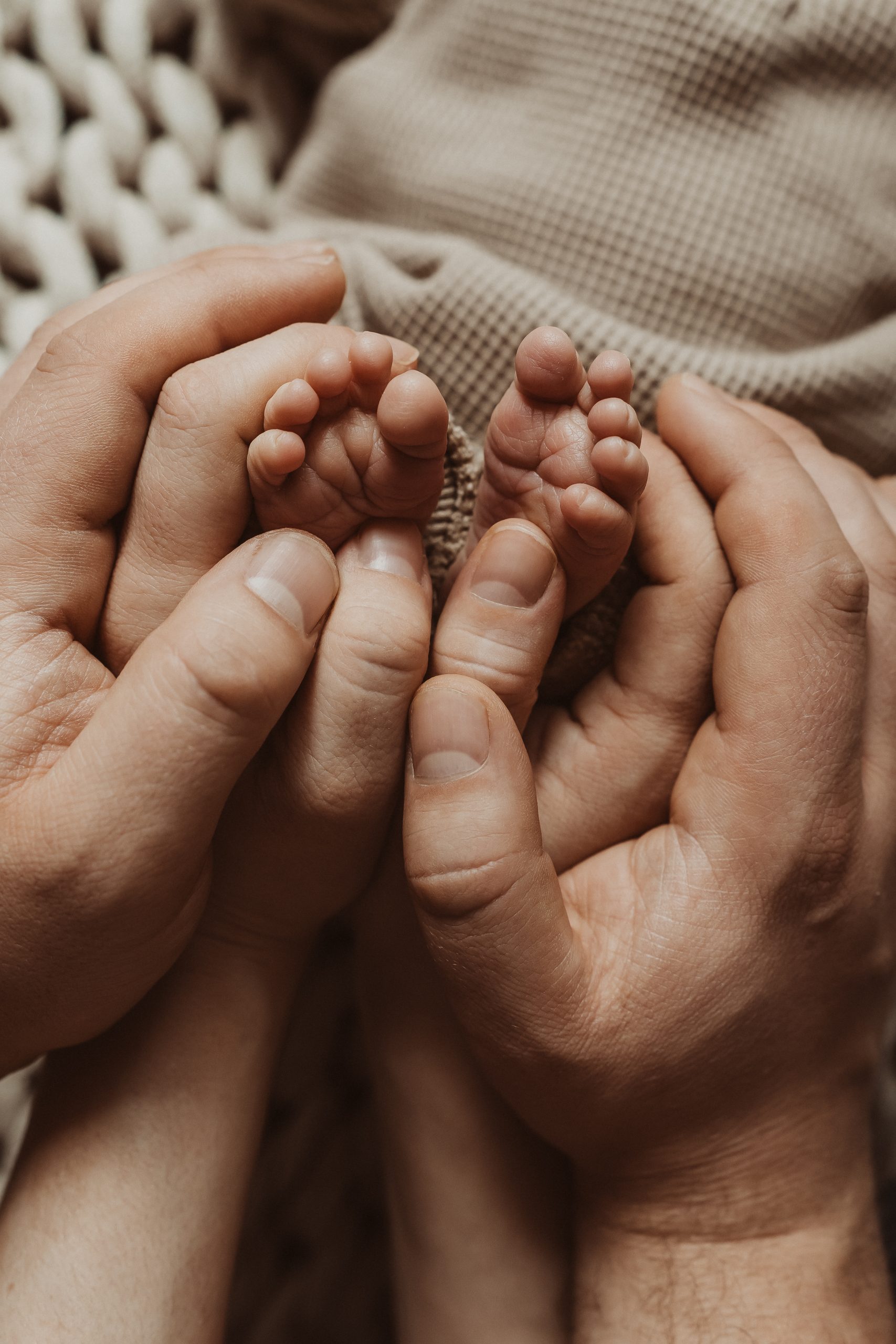 die Eltern halten zusammen die Füße ihres Babys. Dabei liegen die Hände aufeinander