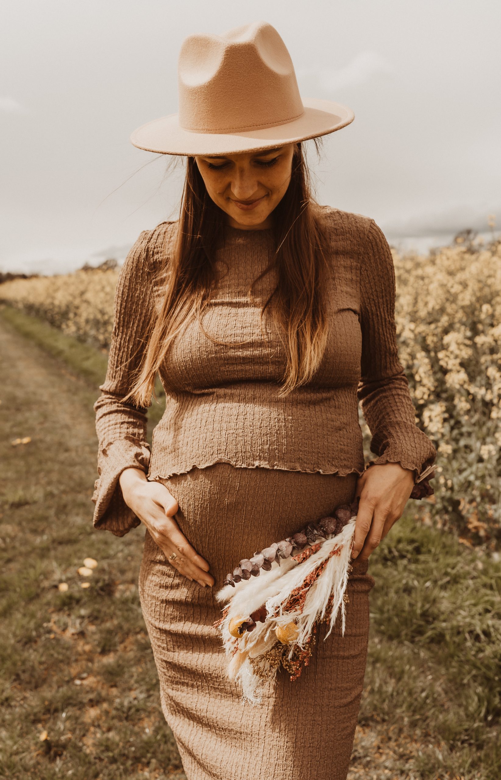 eine werdende Mutter betont ihren Bauch beim Babybauchshooting im Rapsfeld