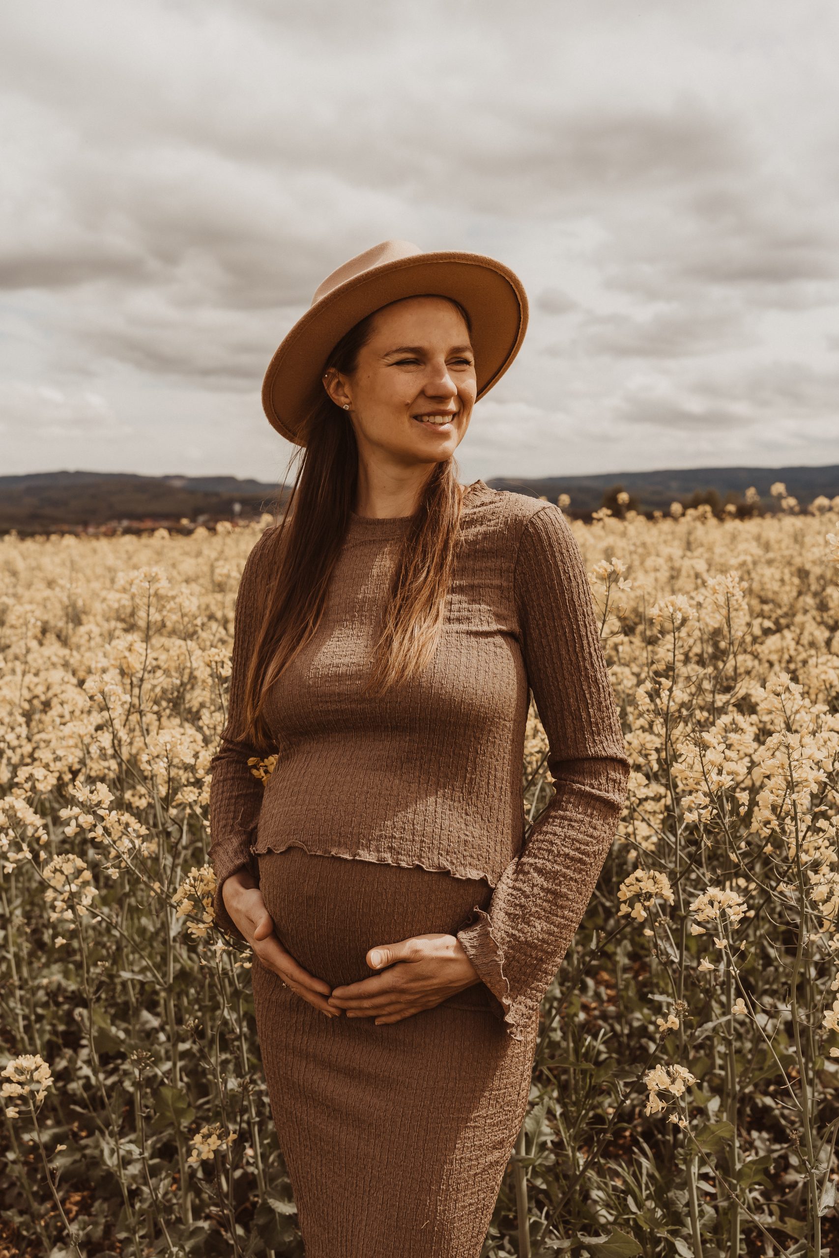 Schwangere mit Hut beim Babybauchshooting im Rapsfeld